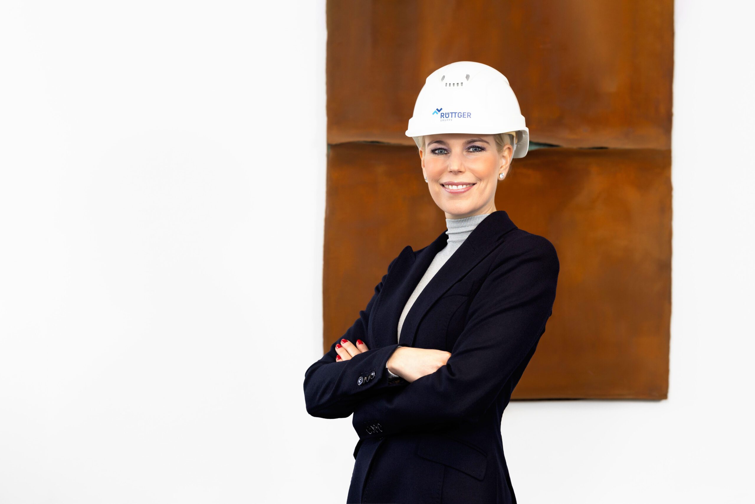 Alt Text: Personal Branding Portrait Lorin Ruettger Architektin Geschaeftsfuehrerin Melsungen schwarze Anzugjacke Rollkragenshirt weisser Schutzhelm verschraenkte Arme laechelnd professionell